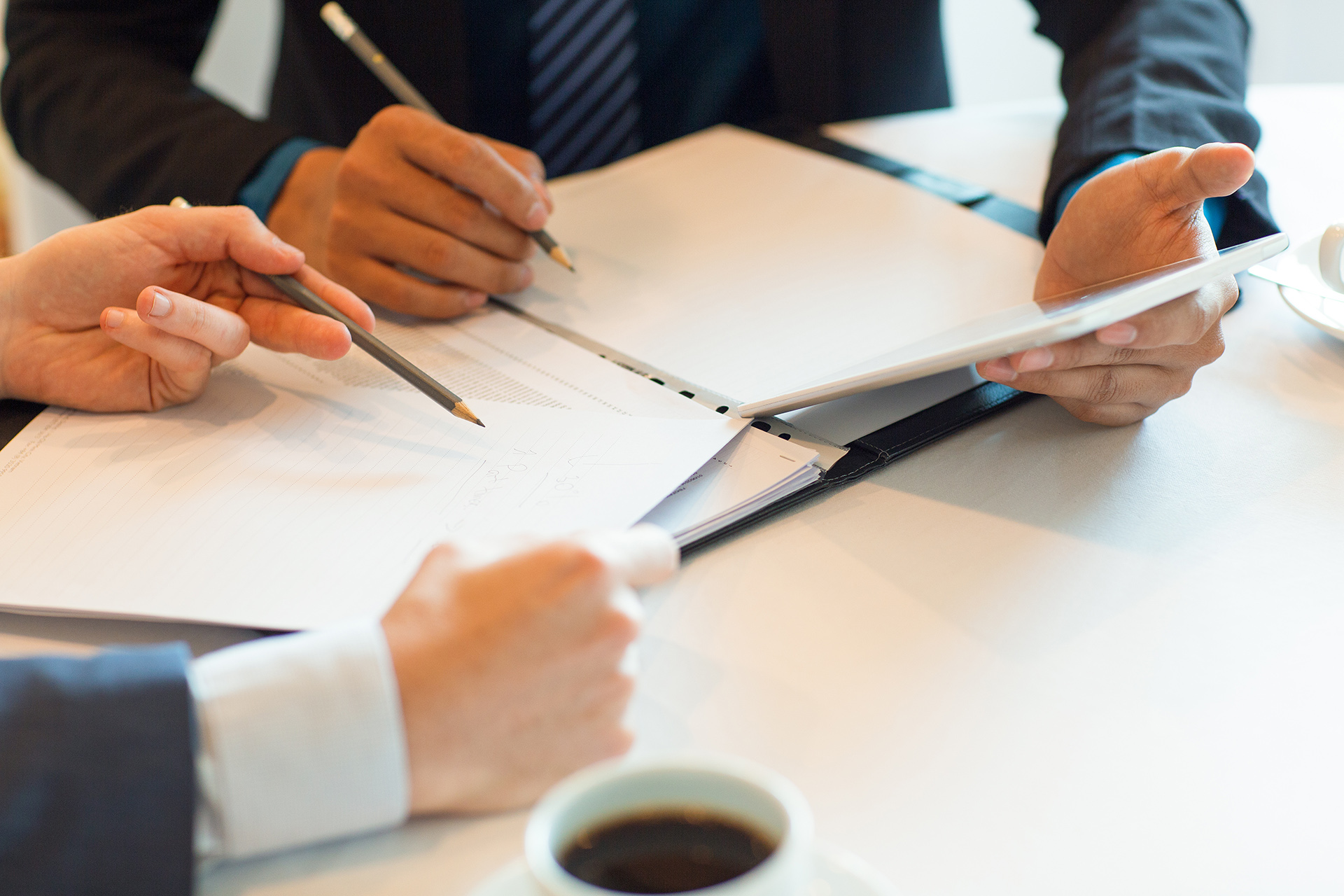 Cropped view of two business men sitting at table and working with documents and information on tablet PC screen